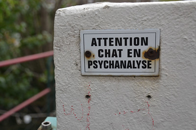 Mur de balcon en béton. Un panneau "Attention chat en psychanalyse est marqué" [Humour]